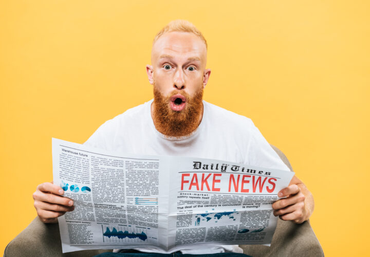 surprised man reading newspaper with fake news while sitting on armchair, isolated on yellow
