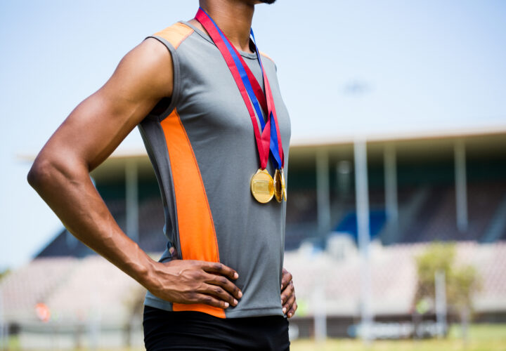 Mid section of athlete posing with gold medals around his neck in stadium